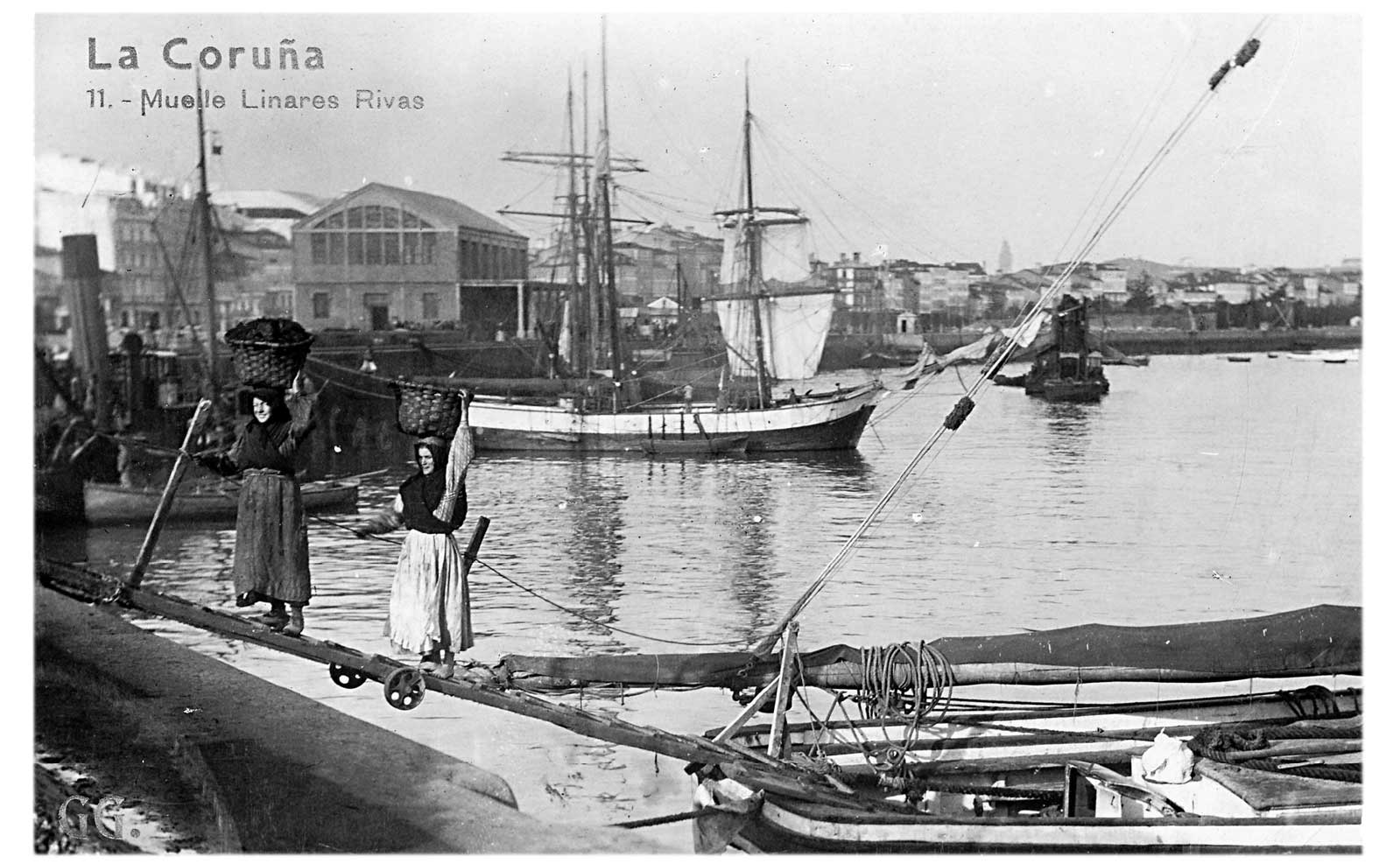 Women carrying loaded baskets on their heads along a plank at the Linares Rivas quay, A Coruña
