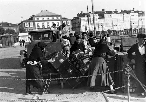 Emigrants loading trunks onto a cart on the quay at A Coruña, the waterfront galleries behind